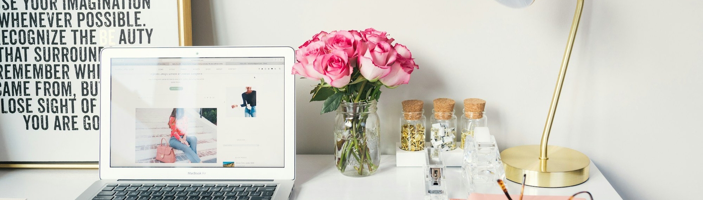 Image of a clean and tidy desk with lamp, laptop, phone, a print nad some roses