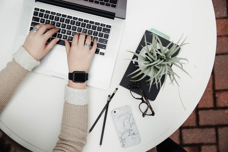 Flat lay of someone typing on a laptop, with a phone, glasses, pencils and plant 
