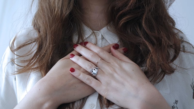 woman wearing silver-colored ring holding her hands over her chest to illustrate self care